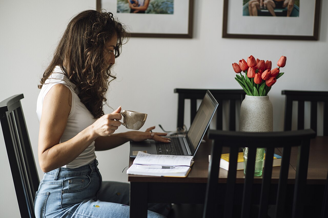 A person working on a laptop at a kitchen table with a coffee